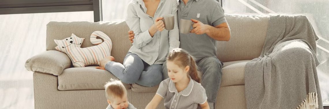 Cheerful family wearing casual clothes sitting in living room while playing and drinking tea during weekend at home in morning