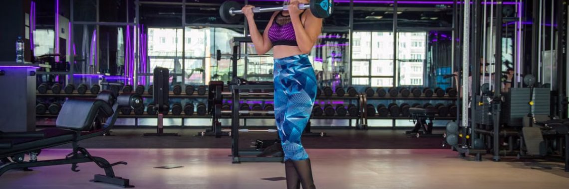 Fit woman lifting barbell in a modern gym with vibrant lighting.